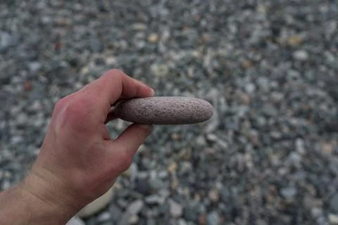 A flat stone in the hand of a man on the background of a stone beach Stock Photos