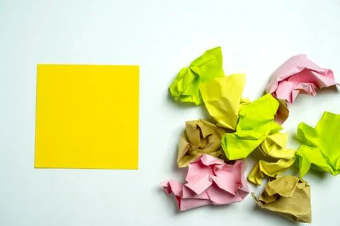 A flat yellow sticky note next to crumpled colored paper balls on a white b.. Stockfoto's