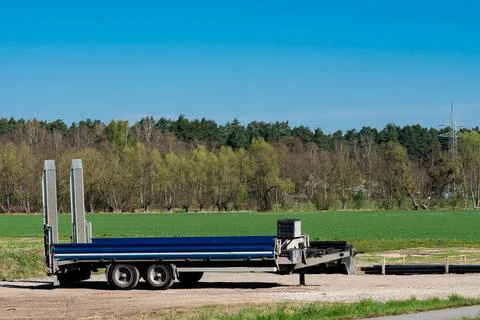 Flatbed trailer parked in an open field under clear blue sky Stock Photos
