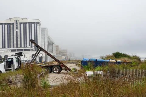 Flatbed truck preparing to load a large dumpster full of oil drums on the bea Foto stock