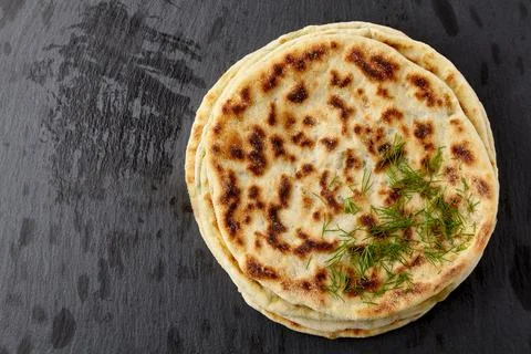 Flatbread with cheese and herbs on a dark stone table Stock Photos