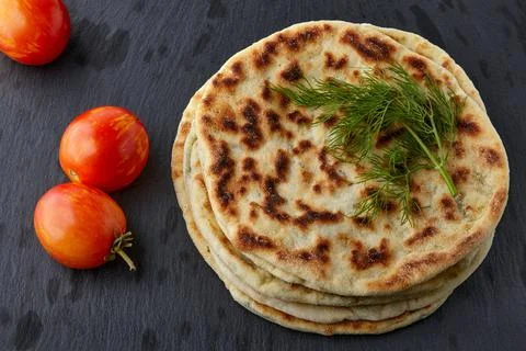 Flatbread with cheese and herbs on a white plate with tomatoes Stock Photos