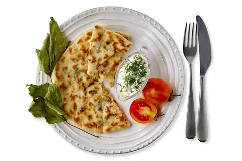 Flatbreads with cheese and herbs and yogurt sauce on a white plate with cutlery Stock Photos