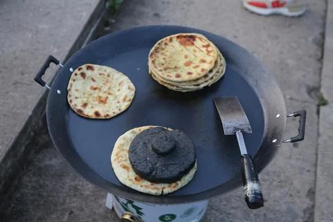 Flatbreads cooking on a large outdoor griddle with spatula and food weight .. Fotos de archivo