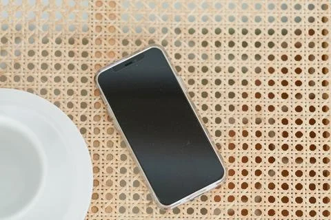 A flatlay of an android phone and a white coffee cup on a rattan Stock Photos
