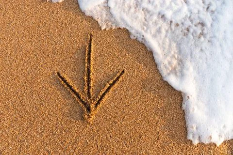Flatlay An arrow drawn on the sand pointing to the left next to sea foam F... Stock Photos