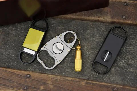 Flatlay Assortment of Cigar Cutters on Rustic Wood Table Beside Cigar Box Stock Photos