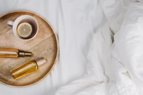 Flatlay of bed with white sheets, blankets and wooden tray with lemon tea and Stock Photos