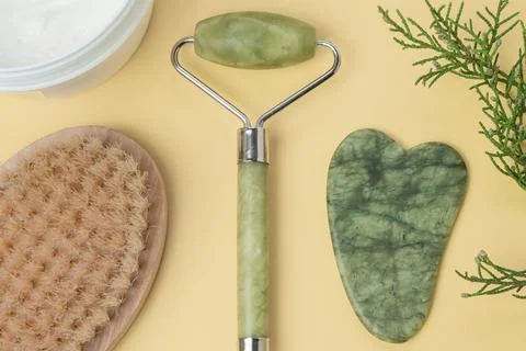 Flatlay with cream, face roller,face gua sha, massage brush on yellow backgro Stock Photos
