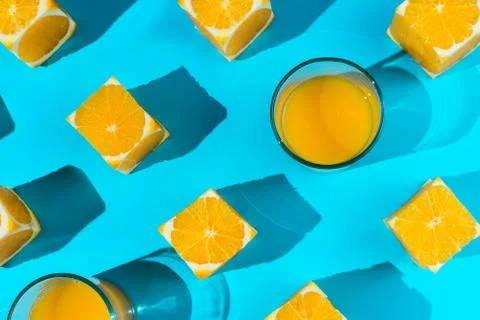 Flatlay of cubes cut out of oranges and glasses with juice on blue Stock-Fotos