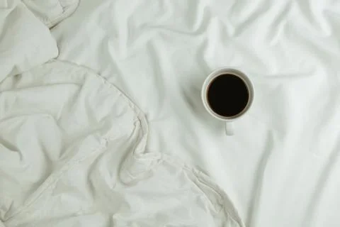 Flatlay of cup of coffee in bed on white sheets, morning concept Stock Photos