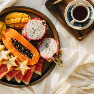 Flatlay with cup of coffee or tea on wooden tray and tropical fruit plate wit Stock Photos