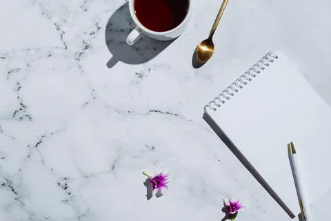 Flatlay of cup of tea, notebook with blank page and pen on marble Stock Photos