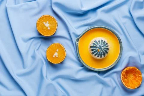 Flatlay of cut oranges and ceramic hand squueze juicer on blue drapery Stock Photos