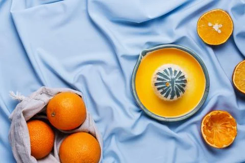 Flatlay of cut oranges and ceramic hand squeeze juicer on blue drapery Stock Photos