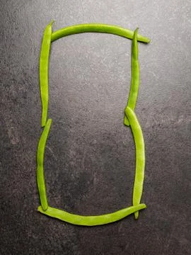 Flatlay of the digit zero laid out with long green beans on dark table 스톡 사진