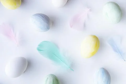 Flatlay of Easter colored eggs and feathers on white background Stock Photos