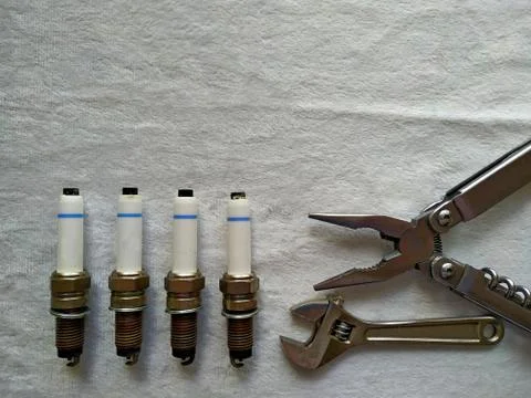 Flatlay of four spark plugs, adjustable spanner and pliers on a white background Stock Photos