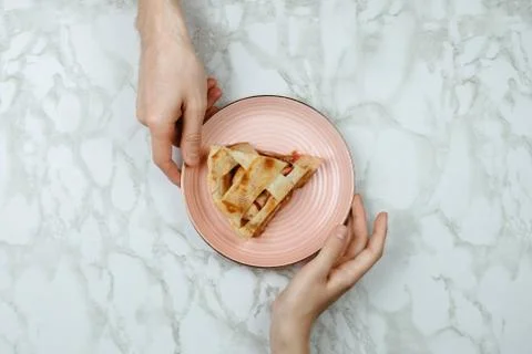 Flatlay of men passing the piece of apple pie to woman's hand on marble backg Stock Photos