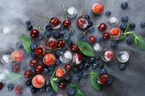 Flatlay of mint, various berries, ice and smoke on dark background, selective Stock Photos