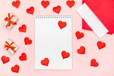 Flatlay notepad mock up with a red envelope with hearts and gifts on a pink b Stock Photos