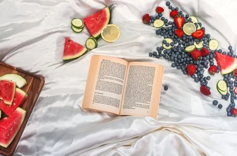 Flatlay of a open book surrounded by fresh fruit on white silk Stock Photos