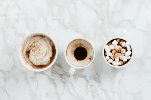 Flatlay of three white cups of vegan cacao with various toppings on marble ba Stock Photos