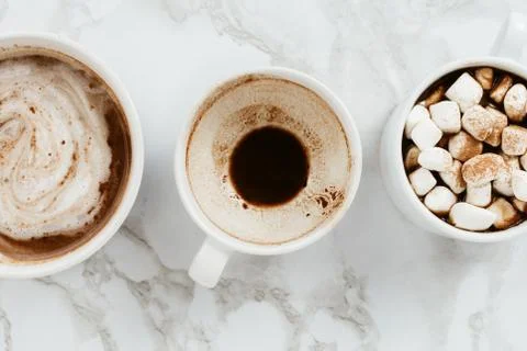 Flatlay of three white cups of vegan cacao with various toppings on marble ba Stock Photos