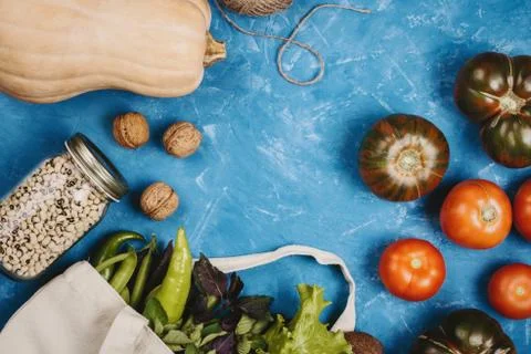 Flatlay of tomatoes, greens, pumpkin, string and beans in a jar on blue backg Stock Photos