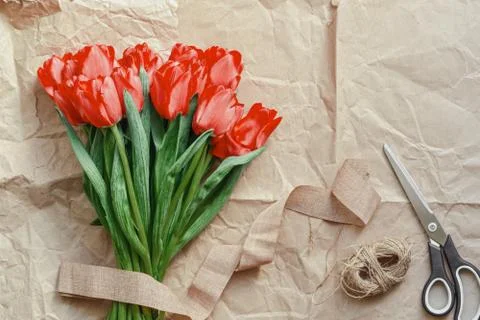Flatlay of tullips and craft wrapping paper, ribbon, scissors and present. Stock Photos