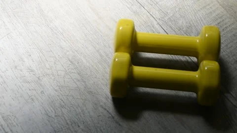 Flatlay of Two Yellow Dumbbells on the Floor and a Hand Reaching for One Stockbeeldmateriaal 245575845