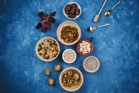 Flatlay of various seeds, nuts and granola in a bowls on blue background Stock Photos