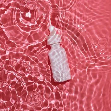 Flatlay of white bottle with serum lying in pink rippling water Stock Photos