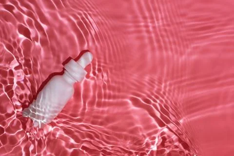 Flatlay of white bottle with serum lying in pink rippling water Stock Photos