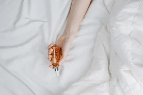 Flatlay of woman's hands in bed holding bottle with serum, beauty and skincar Foto stock
