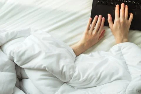 Flatlay of woman's hands covered by blanket on a bed printing on a laptop Stock Photos