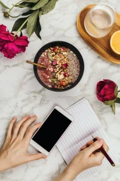 Flatlay of woman's hands with notebook and smartphone, vegan smoothie bowl wi Stock Photos