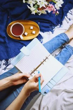 Flatlay with woman's hands writing in a planner on white sheets with cup of t Stock Photos