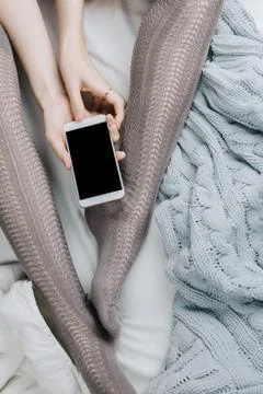 Flatlay of woman's legs in grey stocking holding smartphone with black screen Stock Photos
