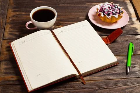 Flatley layout. An open notebook, a green pen, black coffee in a cup and a ca Stock Photos
