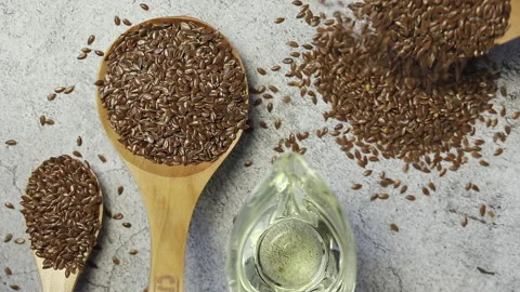 Flax seeds are poured onto the table from a wooden spoon and linseed oil Stock Footage 146318277