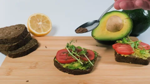 Flax seeds sprinkled onto avocado bread 스톡 동영상 346519196