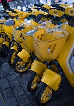 A fleet of modern, bright yellow shared e-bikes equipped with front baskets.. Stock Photos