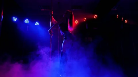 A flexible dancer dances on a pole under the light of colorful spotlights. Stock Footage 205263227