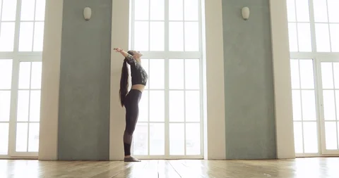 Flexible girl practicing yoga performs asanas in light class near large window. Stock Footage 127102796