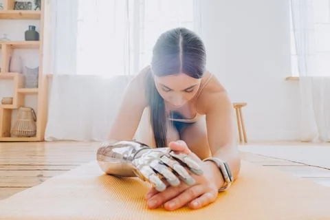 Flexible woman with bionic arm does yoga exercises in room Stock Photos