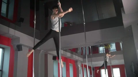 Flexible young man exercising pole dance elements on a pole Stock Footage 89554172