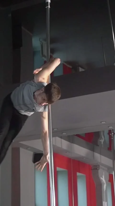 Flexible young man exercising pole dance elements on a pole Stock Footage 346813458