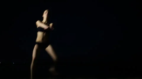 Flexible young woman doing split on black background at night beach Stock Footage 64638550