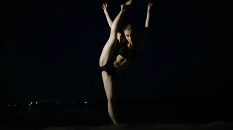 Flexible young woman doing split on black background at night beach Stock Footage 64638554
